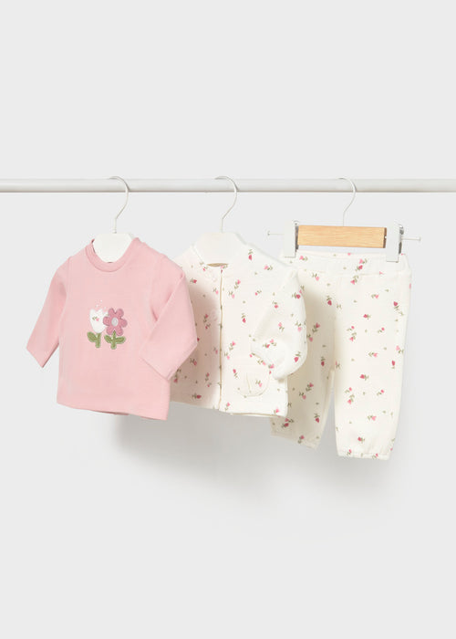 Three-piece infant set with a pink top featuring a flower applique, a white floral jacket, and matching pants.