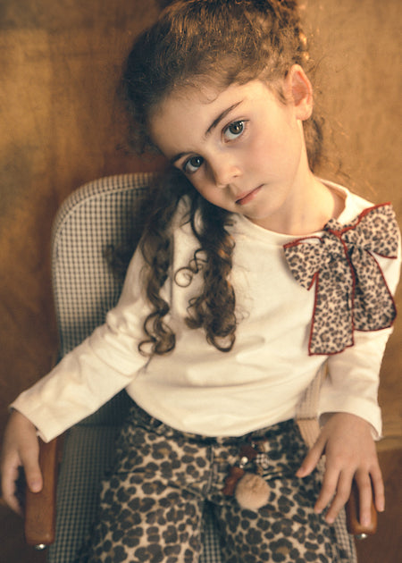 Girl wearing a cream top with a leopard print bow and leopard print denim pants.