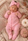 Baby in pink ribbed footie with frill detail and matching headband, lying on a knitted blanket.
